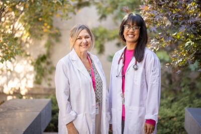 A nurse and doctor stand outside, in white lab coats, smiling