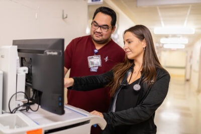 A physician assistant and registered nurse look at a computer monitor.