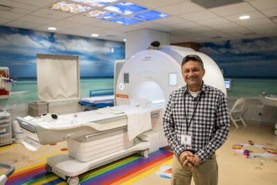 MRI technologist, Sumeet Gupta stands next to the MRI machine.