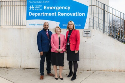 Monrose, Jones and MacArthur standing outdoors in front of a sign promoting the Ontario investment in the General Hospital Emergency Department Renovation.