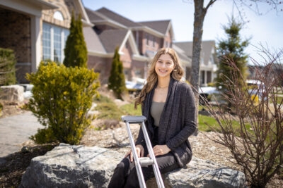 Katie Mantione sitting on stones outside her home, with crutches in hand