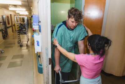 A nurse helps a patient using a walker back into a washroom in an older patient room in Juravinski Hospital.