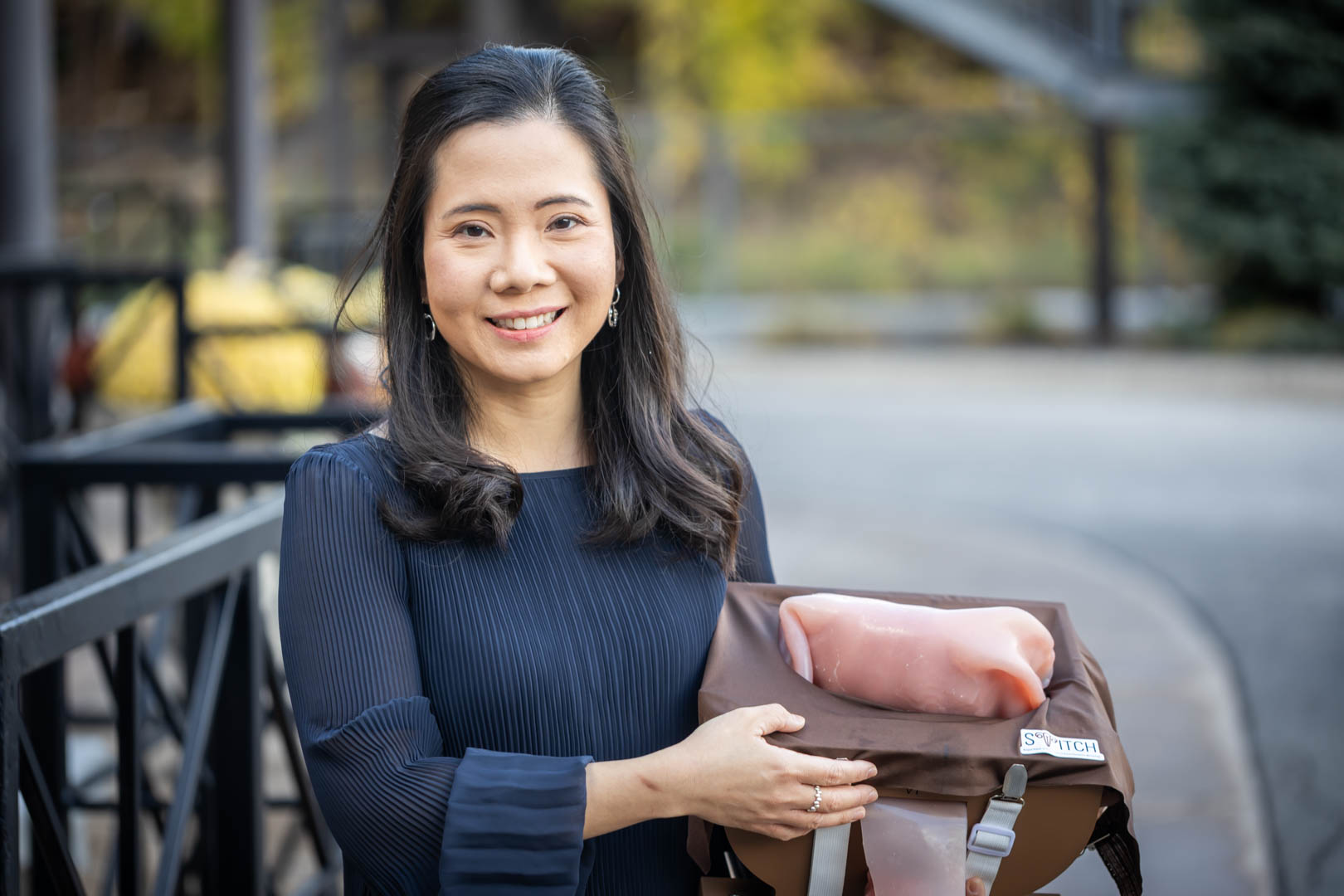 Dr. Esther Chin stands outdoors, smiling, holding a STITCH simulator