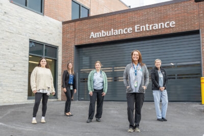 five people stand on a driveway outside the ambulance entrance