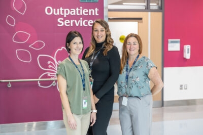 Three people in front of a pink wall with the words "outpatient services"