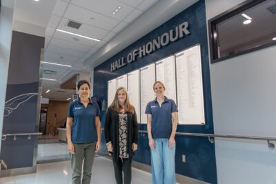 Three people in front of the Wall of Honour
