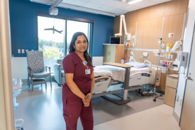 A nurse in burgundy scrubs stands in a patient room